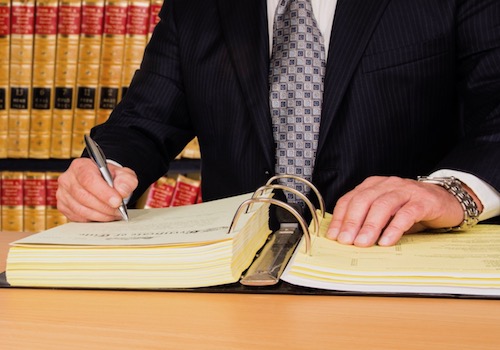 Stock Image of an Attorney in a Law Library Writing in a Large Legal Binder at a Table