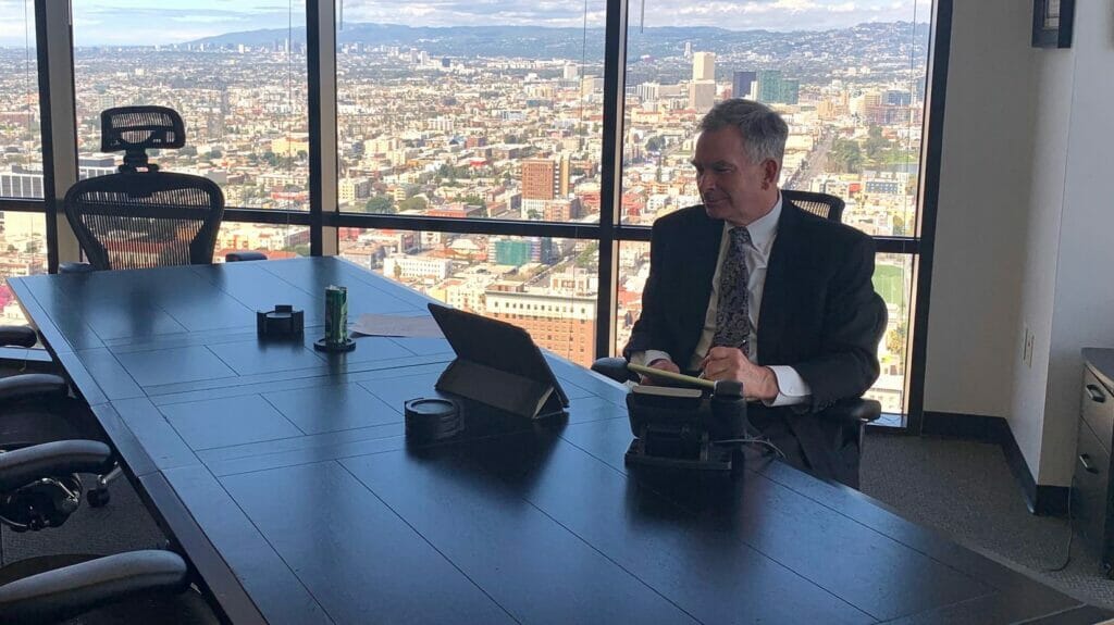 orange county personal injury attorney derek pakiz in office in Orance CA at his desk working and on the phone wearing suit and tie city background