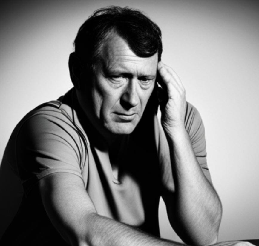 middle aged man sitting at table with a brain injury touching is head black and white