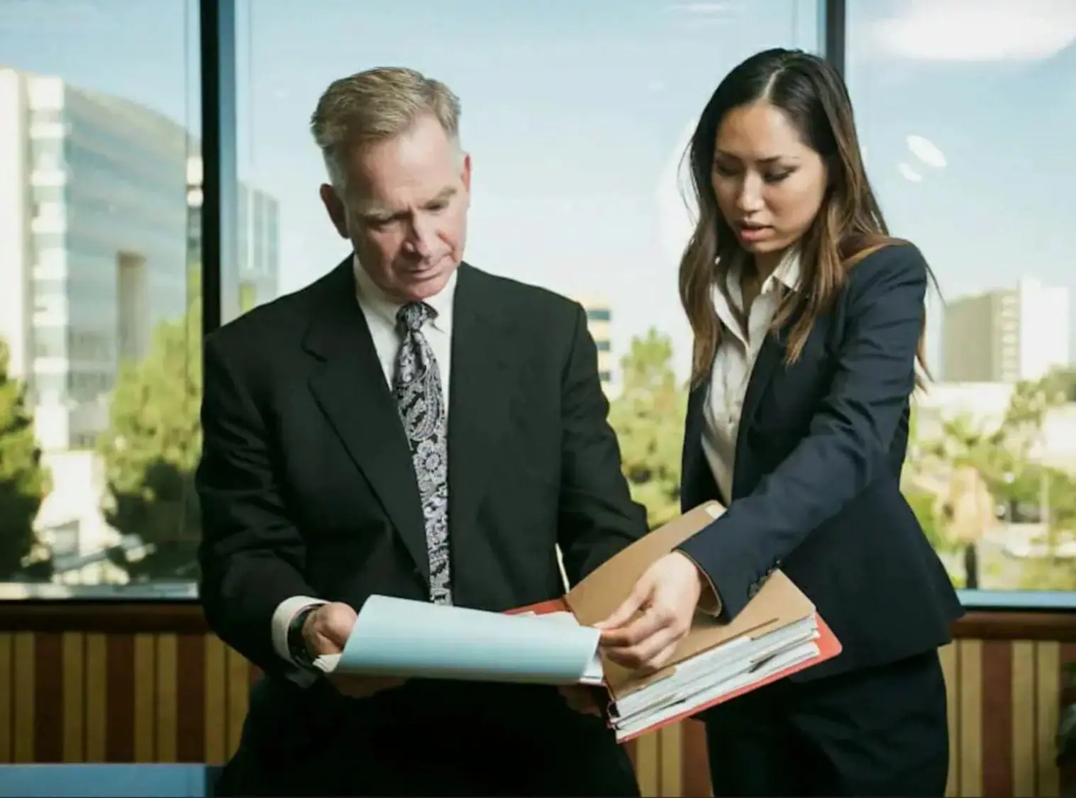 attorney derek pakiz and paralegal caroline la in suits in front of window in san bernardino